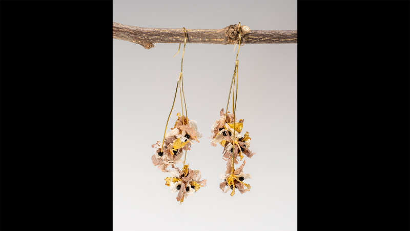 A pair of earrings made from wood shavings dangle from a tree branch.