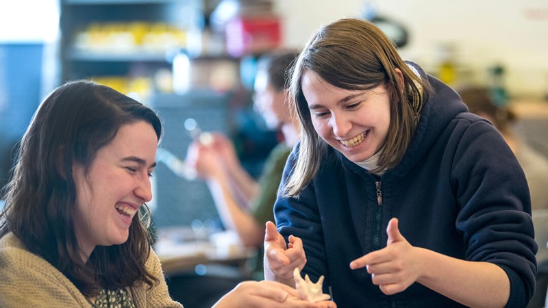 two students laugh as one holds a small shell-like object.