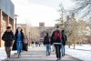 students walk on path outdoors with snow, wearing masks