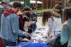 students line up along a table, gathering items to decorate their graduation caps.