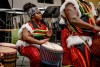 student wearing traditional African clothing playing a drum.