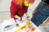 student working at a table with a level, tape measure, pushpins and box of markers.