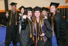 six college students wearing graduation regalia posing for a group photo.