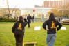 two college students facing away from the camera throwing a beanbag in the air while playing corn hole.