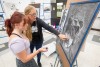 high school art student standing next to college professor who is pointing to the eyes of a self-portrait done in charcoal.