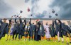 A group of 2024 graduates throw their mortarboards in the air.