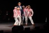 Barbershop quartet sings around suited man on stage