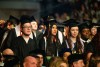 Graduates in cap and gown listen to a speaker
