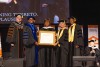 A group of people in academic regalia stand on stage, with one holding an honorary diploma