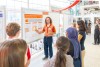 A student stands in front of a research poster with bystanders listening on.