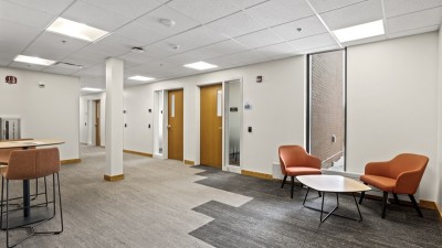 a common area with tables and chairs that leads to a hallway with offices.