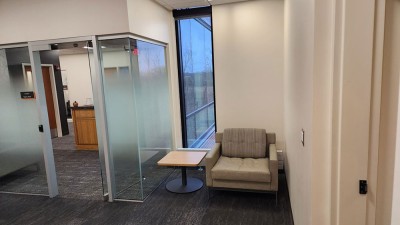 a corner next to a glass office, with a chair and end table.