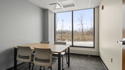 a meeting room with a table and four chairs, and a large window.