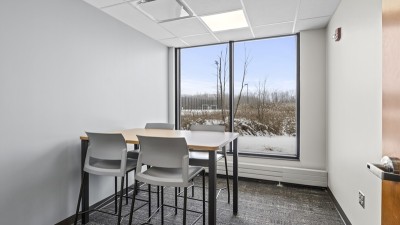 a meeting room with a table and four chairs, and a large window.