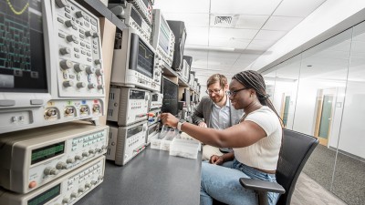 A student using equipment as a professor observes.