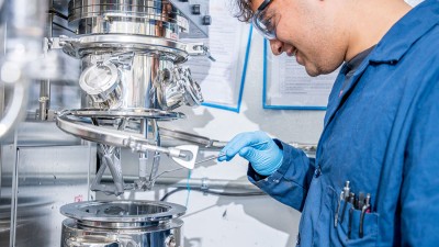 A student wearing a blue lab coat and working with a machine in the R I T Battery Development Center