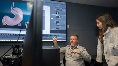professor talks to a student in a lab with a large screen showing a digital image of a stomach.