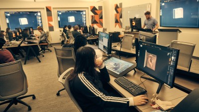 classroom with students working at computer stations with monitors and tablets to draw on.