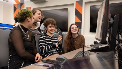students smile and laugh as they look at a computer in a lab.