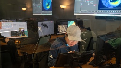 A student works at a computer behind transparent glass.