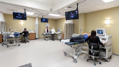 a hospital room with 3 patients all using ultrasound scanners with TVs on the wall showing the scan imagery