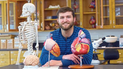 Student sits in lab with models of brain, heart and human skeleton