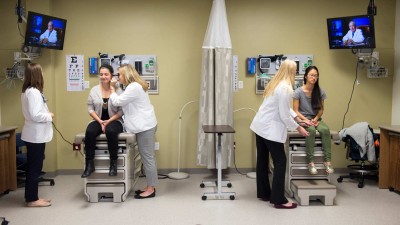 Patients sitting on medical tables in a mock exam room receiving examinations