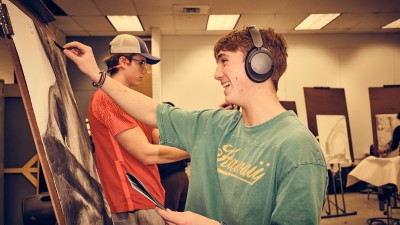 A smiling student draws at an easel.