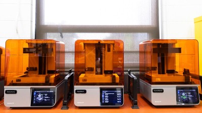 A row of 3D printers with orange-tinted exterior.