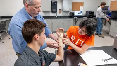 A teacher and student work with a molding/brace of a third person's wrist.