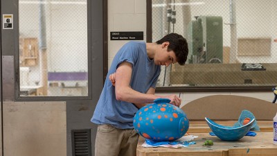 student paints a round piece blue with orange speckles.