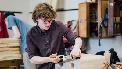 student uses a hand planer on a piece of wooden furniture.