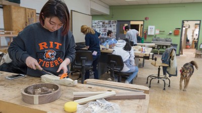 student works on a wood piece using a clamp and chisel.