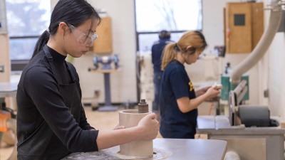 student uses a sander on the inside of a round, hollow wood piece.