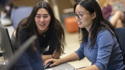Two students smile while using a computer.
