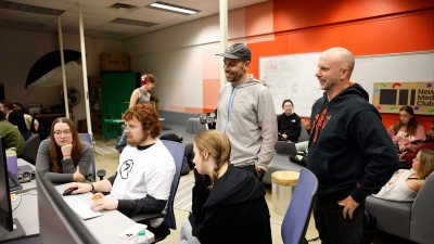 Faculty observe a group of students working at a computer station.