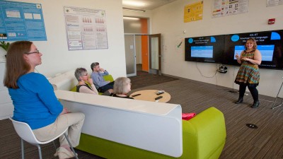 People on a couch watching a presentation on two televisions