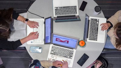 four students at a round table with laptops collaborating