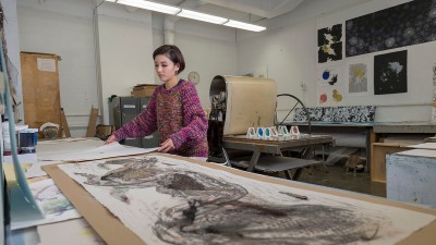student lays out large sheets of paper on a work surface.