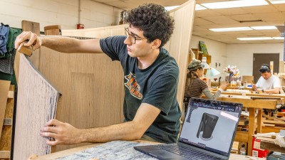 An R I T furniture design student sands a curving wooden art piece.