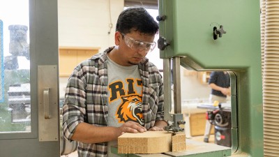 student shapes a piece of wood with a saw.
