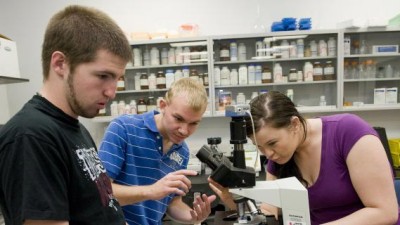 3 people adjusting a microscope in a lab