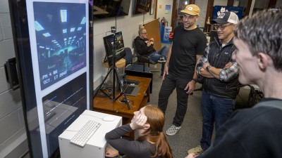 A group of students and faculty gather around a digital display.