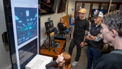 A group of students and faculty gather around a digital display.