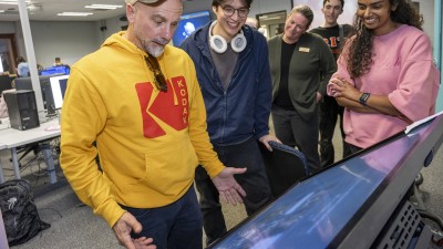 Faculty Jason Arena, surrounded by students, interacts with a large touchscreen.