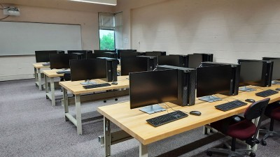 A computer lab with rows of tables with computers and chairs.