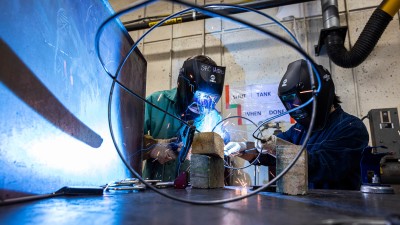 two students wearing protective gear weld a scultpture.