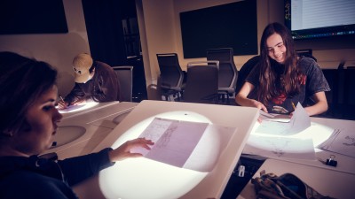 Smiling students draw on light tables.
