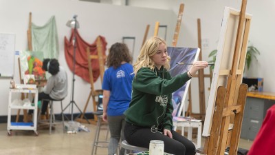 Students paint on canvases on easels in a painting studio.