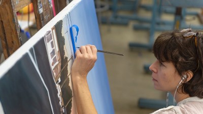 closeup of a student painting powerlines in a landscape.